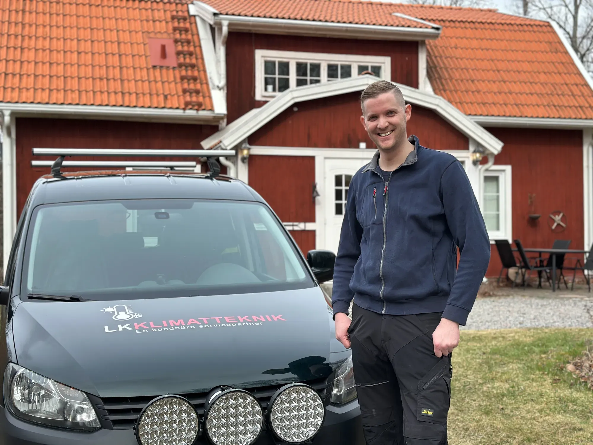 Installatör från LK Klimatteknik vid den märkta servicebilen framför ett rött hus